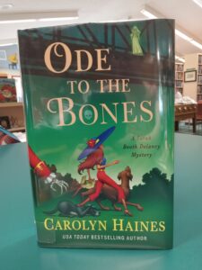 Cover for 'Ode to the Bones', with a woman and dog looking up at a ghostly figure on a bridge, while a second dog cowers as a skeleton hand reaches towards it