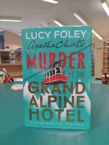 photo of the cover for the mystery novel 'Murder at the Grand Alpine Hotel', featuring a red cable car with mountains in the background