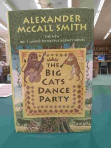 Photo of the cover for the mystery novel 'The Big Cat's Dance Party', Featuring a lion and leopard playing instruments, with a tree and the savannah in the background